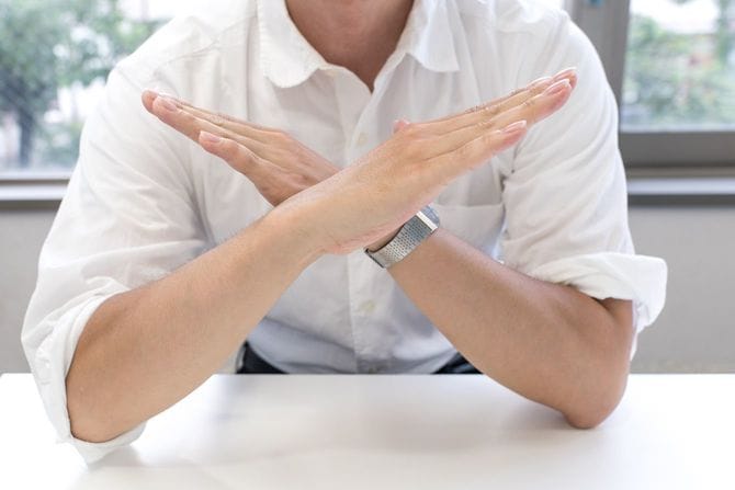 胸の前で腕でバツ印をつくって拒否するジェスチャーをしている