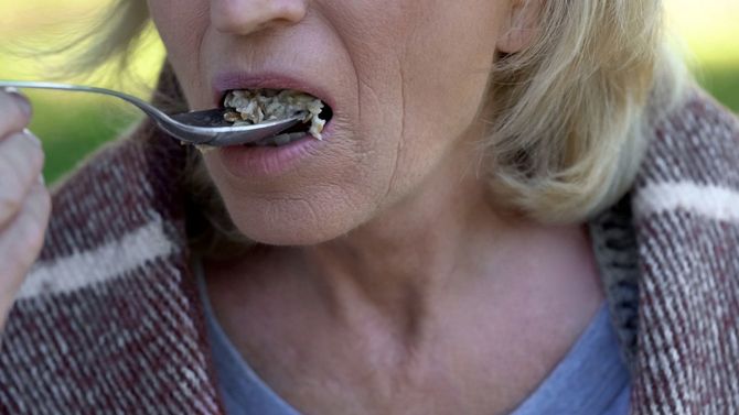 おかゆを口に運ぶシニア女性