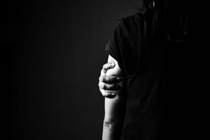 自分の腕をぎゅっと握り、こらえている女性