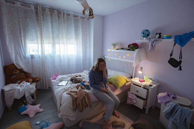 荒れた部屋のベッドに座って思い悩む女の子