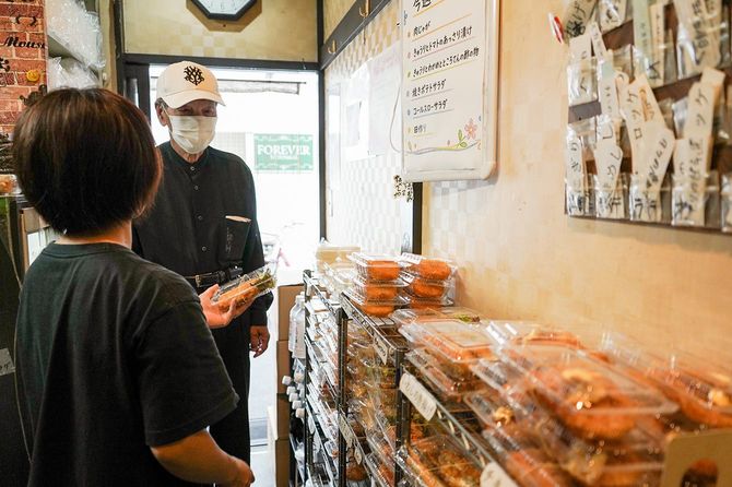 常連客の高齢者に惣菜を説明するボランティアスタッフ