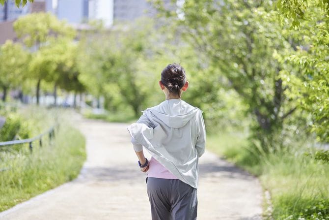 春の新緑の中でランニングを楽しむスポーツウェアを着た女性の後ろ姿