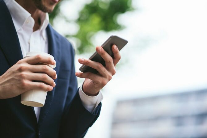 スマートフォンを使い、オフィスの外でコーヒーを飲むビジネスマン