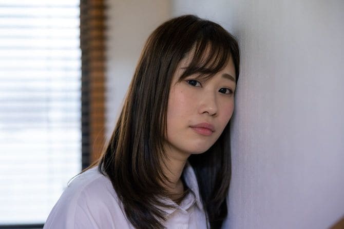 壁に寄りかかってカメラを見る女性