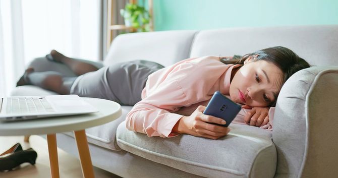 ソファに横たわってスマホを見ている女性
