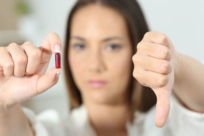 親指を下げて薬を見せる女性