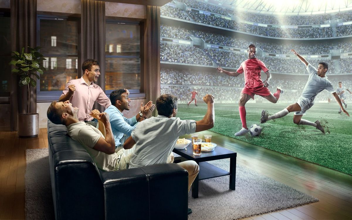 家の壁一面に映ったサッカーのリアルなテレビ中継に熱狂する人たち