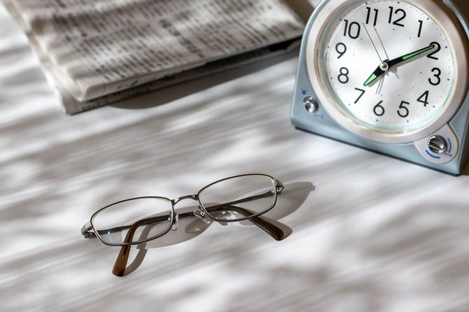 窓のそばの机の上にあるめがね、時計、新聞