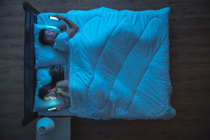 ベッドに入り、それぞれのスマホに没頭するカップル