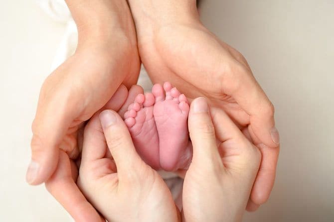 新生児の小さな足を両親が手でそっと包んでいる