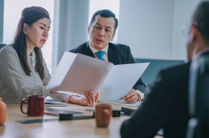 秘書が持っている書類を読む部長