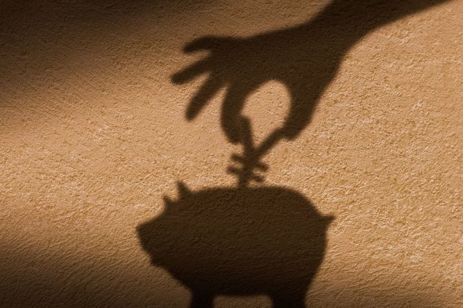 手の影が貯金箱に硬貨を入れる