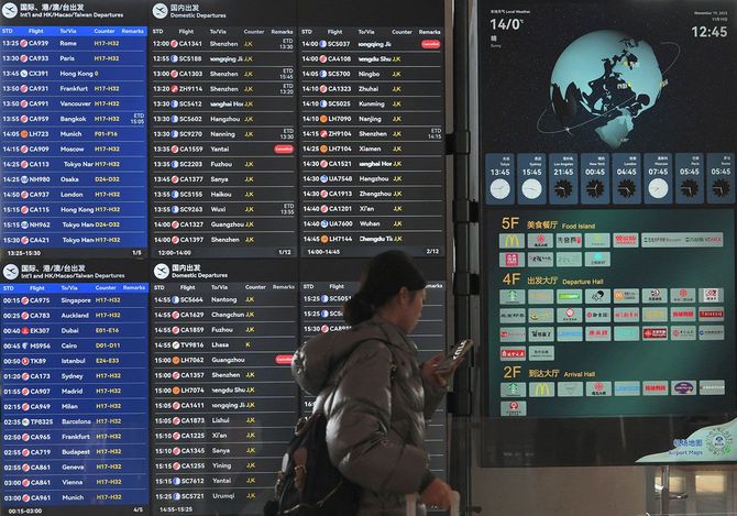 北京首都国際空港で日本行きの便を含む国際線を表示する掲示板の前を通り過ぎる乗客=2025年11月19日