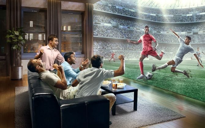 家の壁一面に映ったサッカーのリアルなテレビ中継に熱狂する人たち