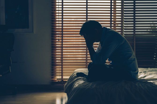 ベッドの上で頭を抱えてうずくまっている男性