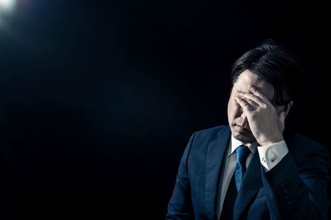 苦悩して目のあたりを手でもんでいる男性