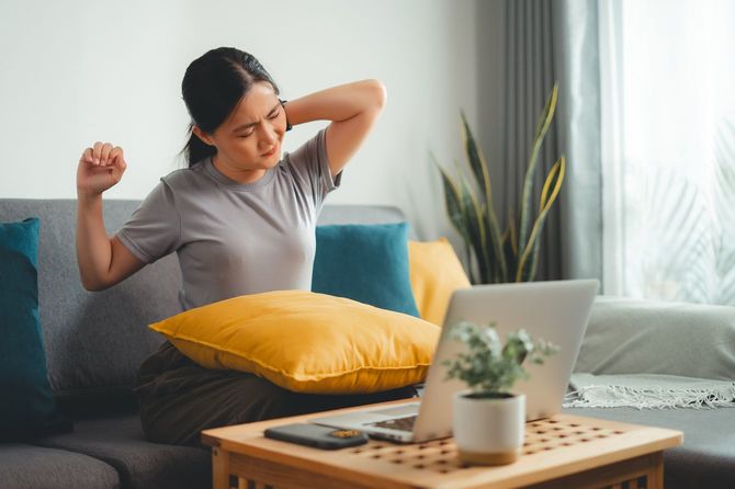 ソファに座って体の痛みに苦しむ女性