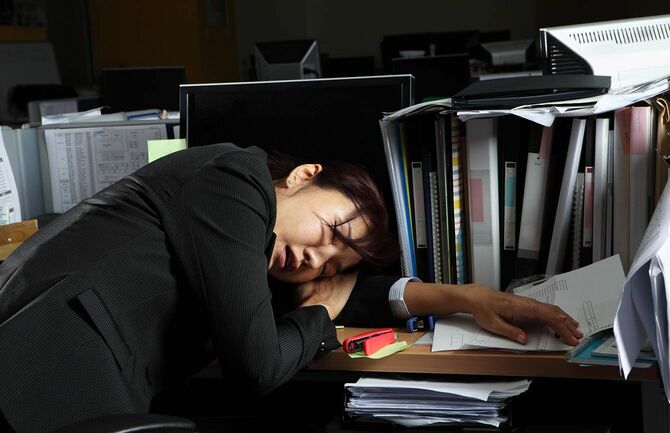 オフィスの机に突っ伏して寝ている女性