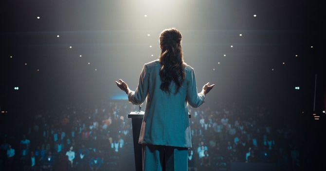 大会場の国際会議で壇上に立ちスピーチしている女性の後ろ姿