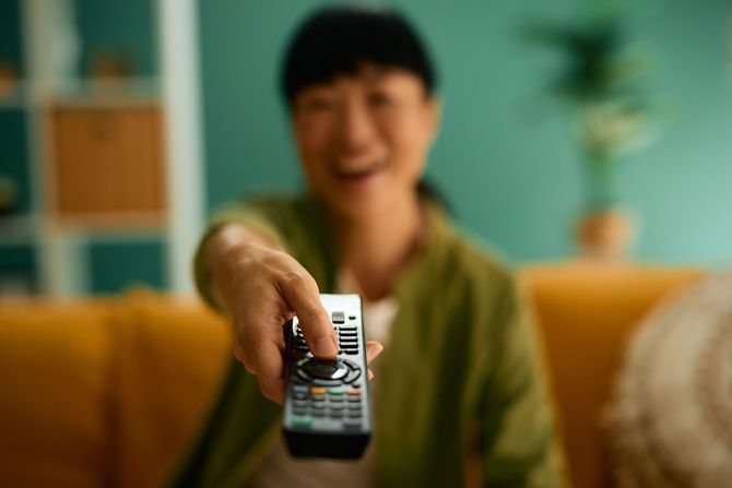 リモコンを持ち、チャンネルを変えてテレビを楽しむ女性