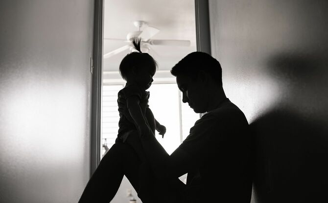 家の床に女の赤ちゃんと一緒に座っている悲しい父親。
