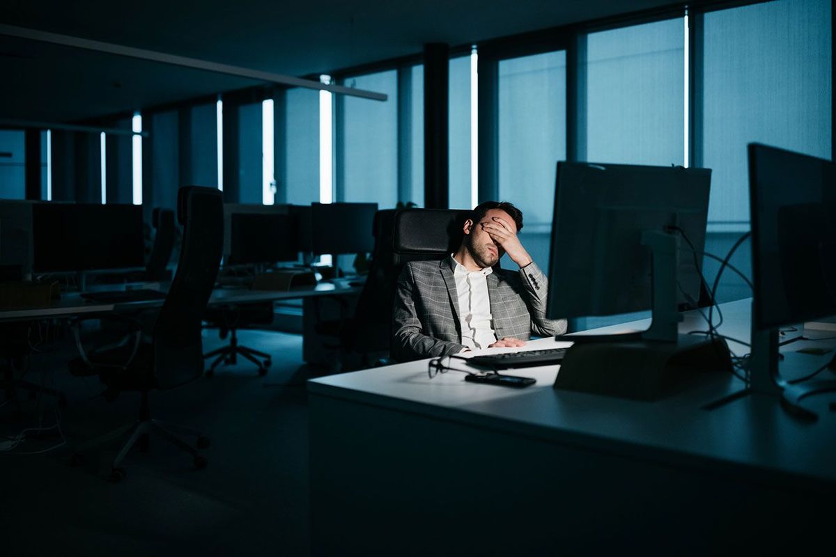 夜のオフィスのデスクで疲れて顔を覆っているビジネスマン