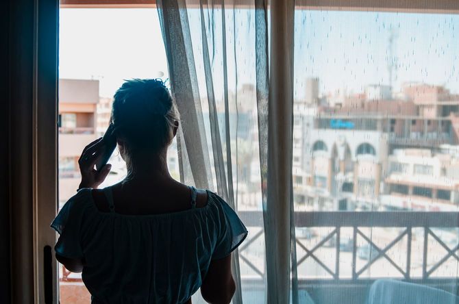 窓から外を眺めながら通話する女性の後ろ姿