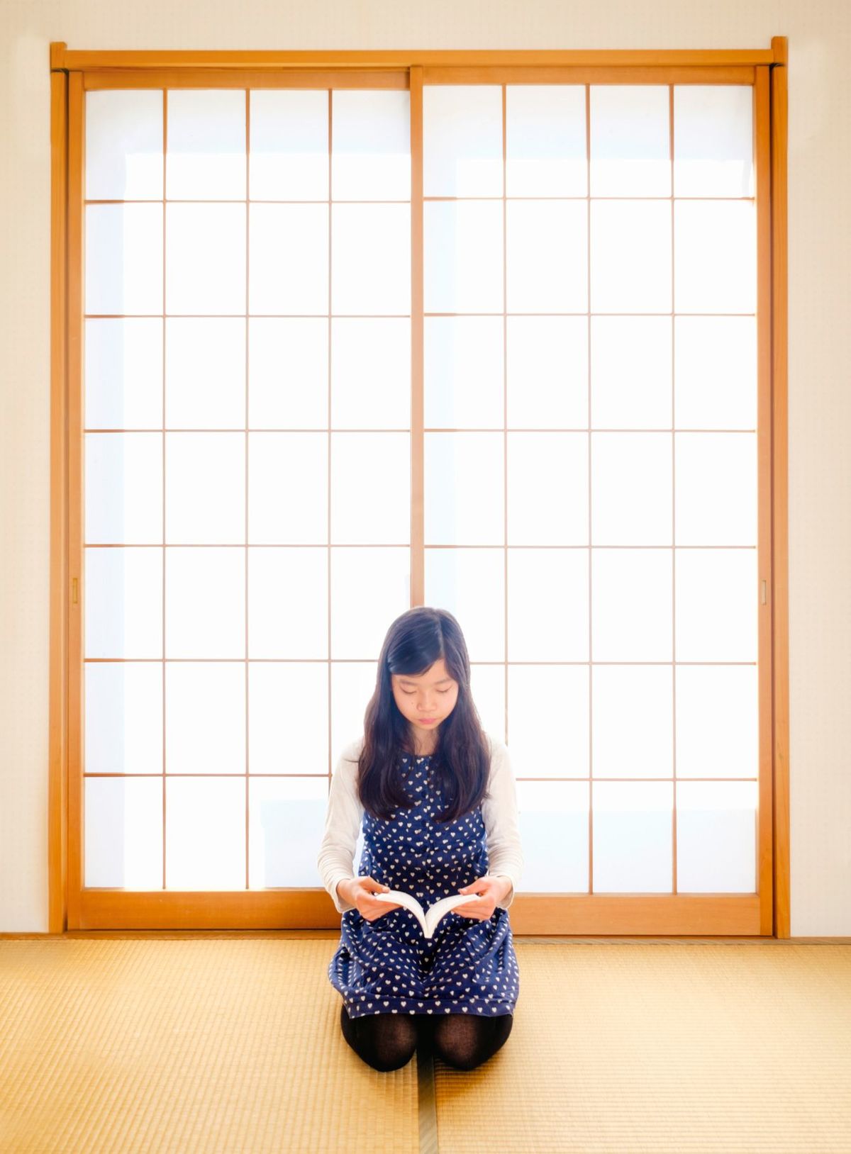 和室の障子の前で正座して本を読む女性