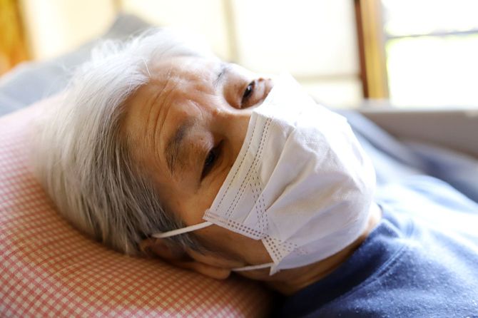 マスクで介護ベッドに横たわっているシニア女性