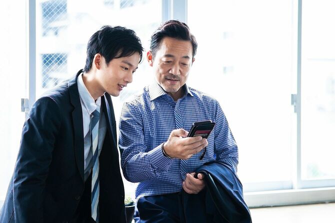 2人のスーツビジネスマンがオフィスの窓際にスマートフォンと会議をしている