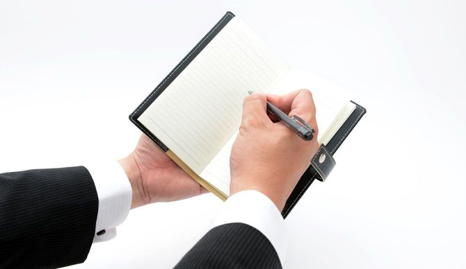 手帳にメモを取る男性の手元