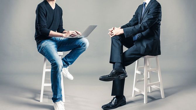 向かい合って座るスーツの男性とカジュアルなスタイルの男性