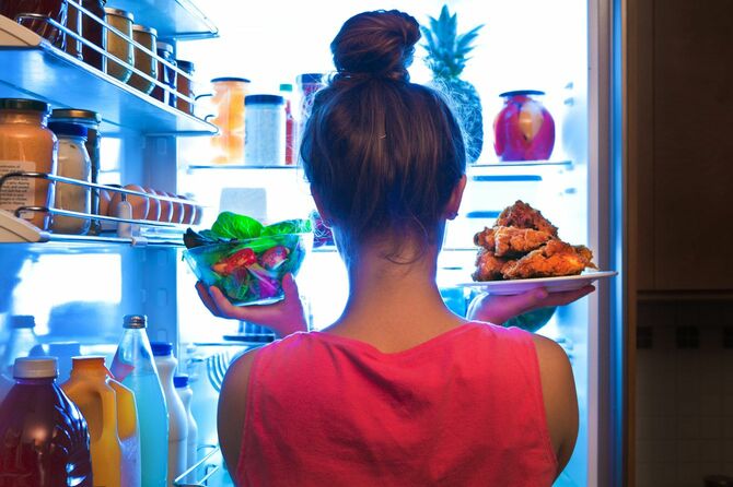 冷蔵庫の前でサラダとチキンを持っている女性