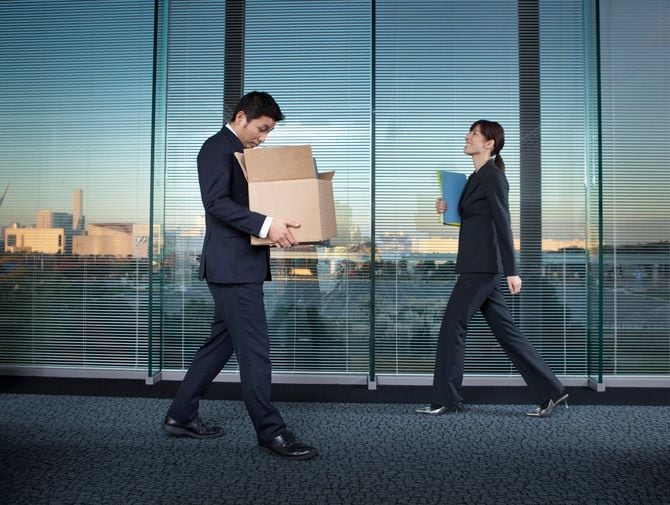 解雇され、段ボールを抱えてうつむきながら歩く男性とすれ違う、笑顔の女性社員