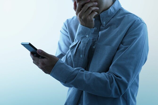 ショックを受けた表情でスマートフォンを見ている男