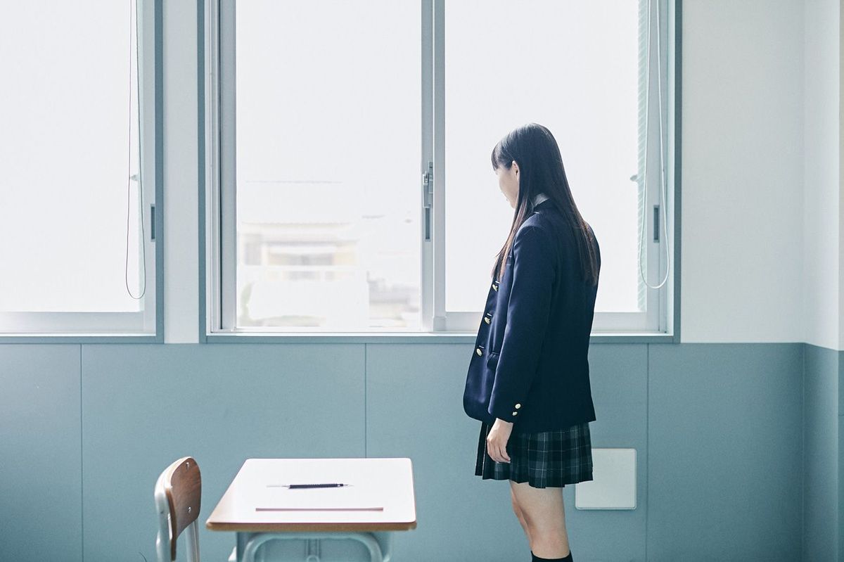 教室の窓際に立つ女子高校生