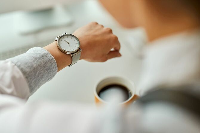 オフィスでコーヒーブレイクをしながら腕時計を見ているビジネスウーマンのクローズアップ。