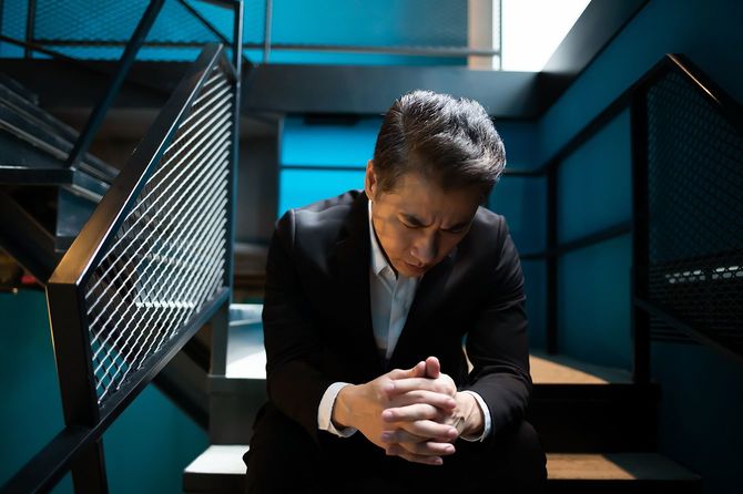 アジアの上級ビジネスマンは動揺し、階段に座っています