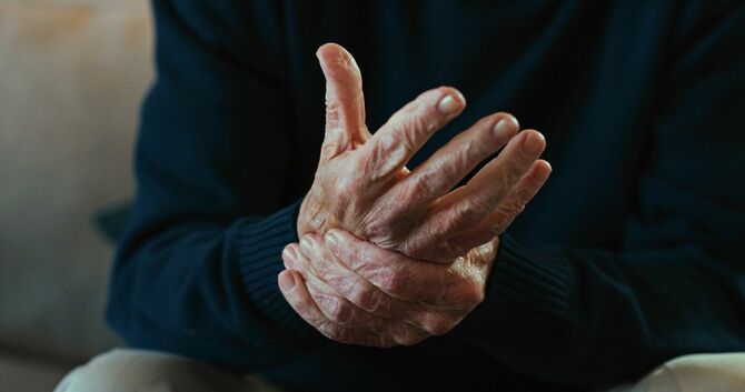 座って手の関節炎に苦しむ高齢男性