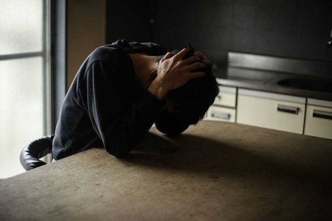 頭を抱えて机にうずくまる男性