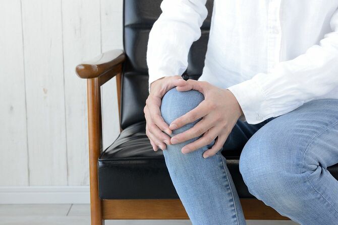 リビングルームで痛みを伴う膝を保持している女性