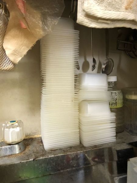 写真H：台所には豆腐パックがきれいに洗われて何十個と積み重ねてあった。