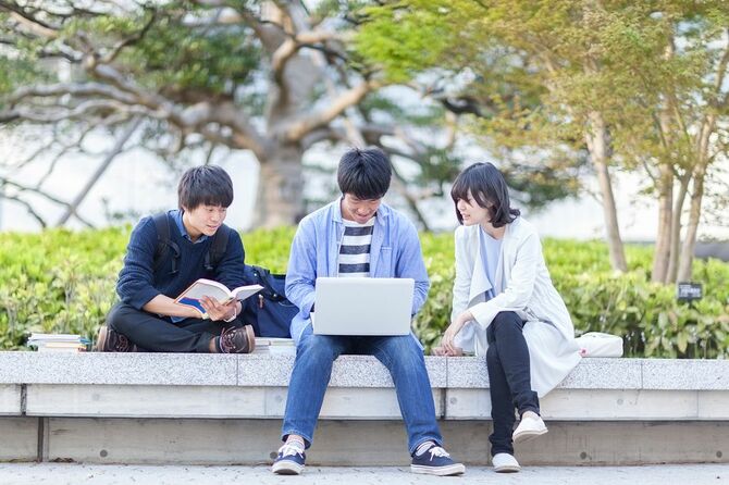 日本の若い大学生のグループが、屋外でノートパソコンで勉強しています。