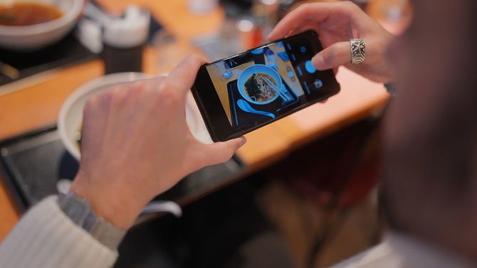 スマートフォンでラーメンの写真を撮る男性観光客
