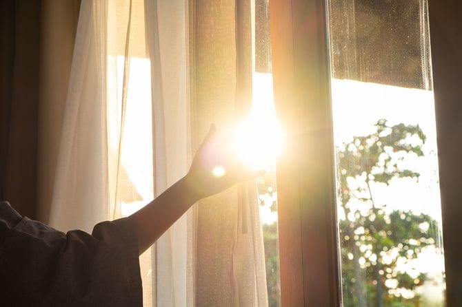 女性の手が寝室の窓の白いカーテンを開けます
