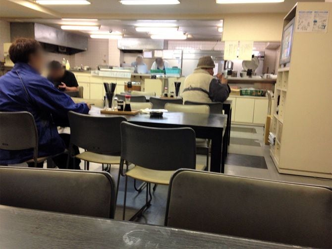 飯場の食堂で夕飯を食べるかっちゃん（右）