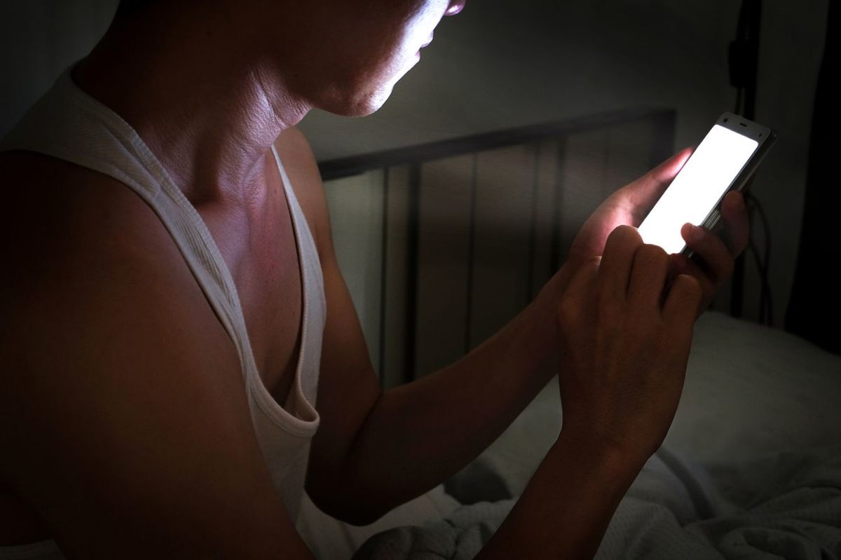 寝室の闇の中で携帯を使用する人
