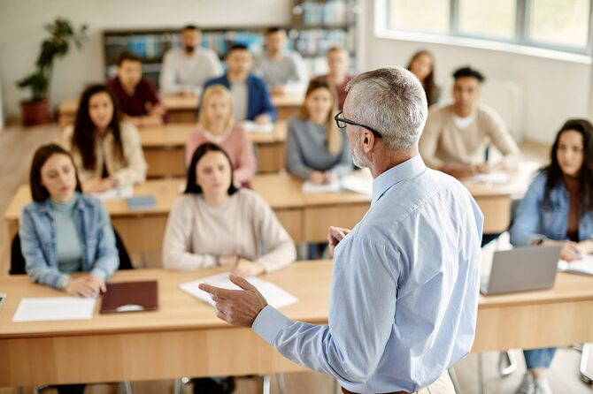 大学の教室での講義中に生徒と話す成熟した教師の背面図。
