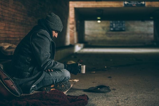 地下道トンネルに座り込み、寒そうにしている男性はステンレスマグを手にしている