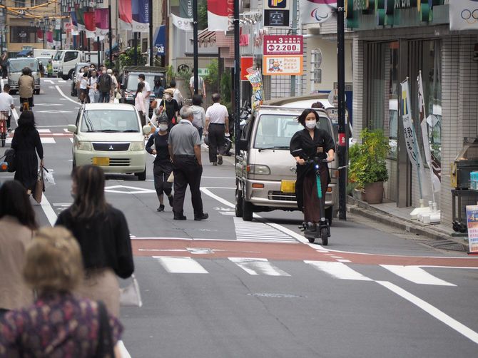 ヘルメットなしで自動車の前を走る電動キックボード